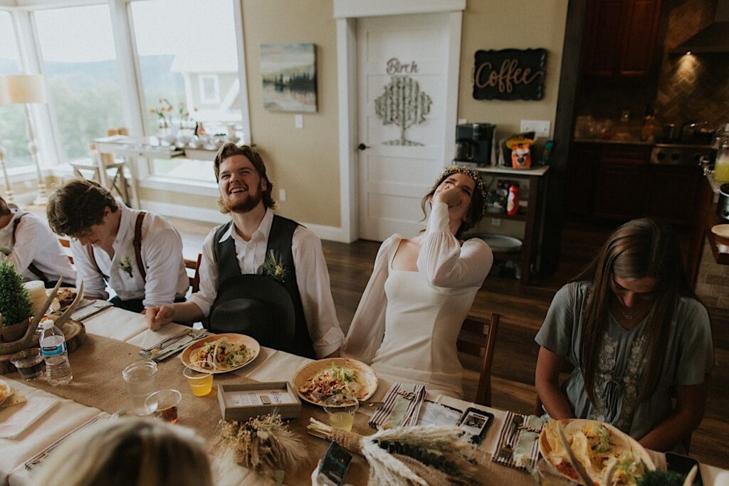 A bride and groom hold hands and laugh while seated at a table with guests of their intimate destination wedding in Tennessee
