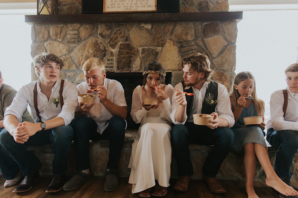 A bride and groom sit on a fireplace with their guests as they eat ice cream together after their intimate destination wedding in Tennessee