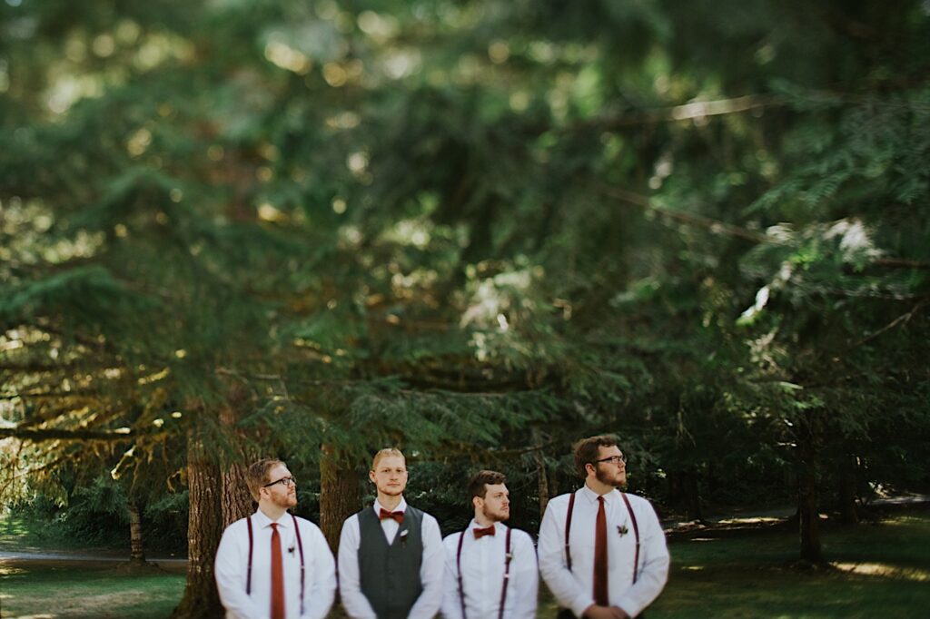 A groom and 3 groomsmen stand side by side in a forest outside of their Airbnb prior to the groom's elopement ceremony