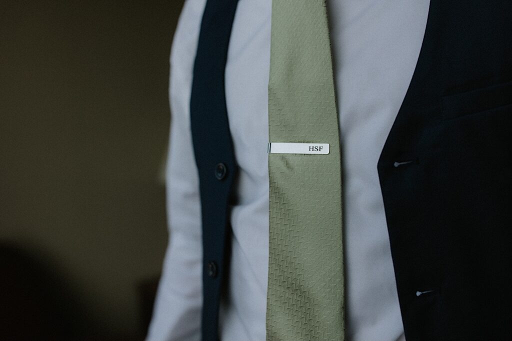 A tie clip reads "HSF" and rests on a green tie that a man is wearing