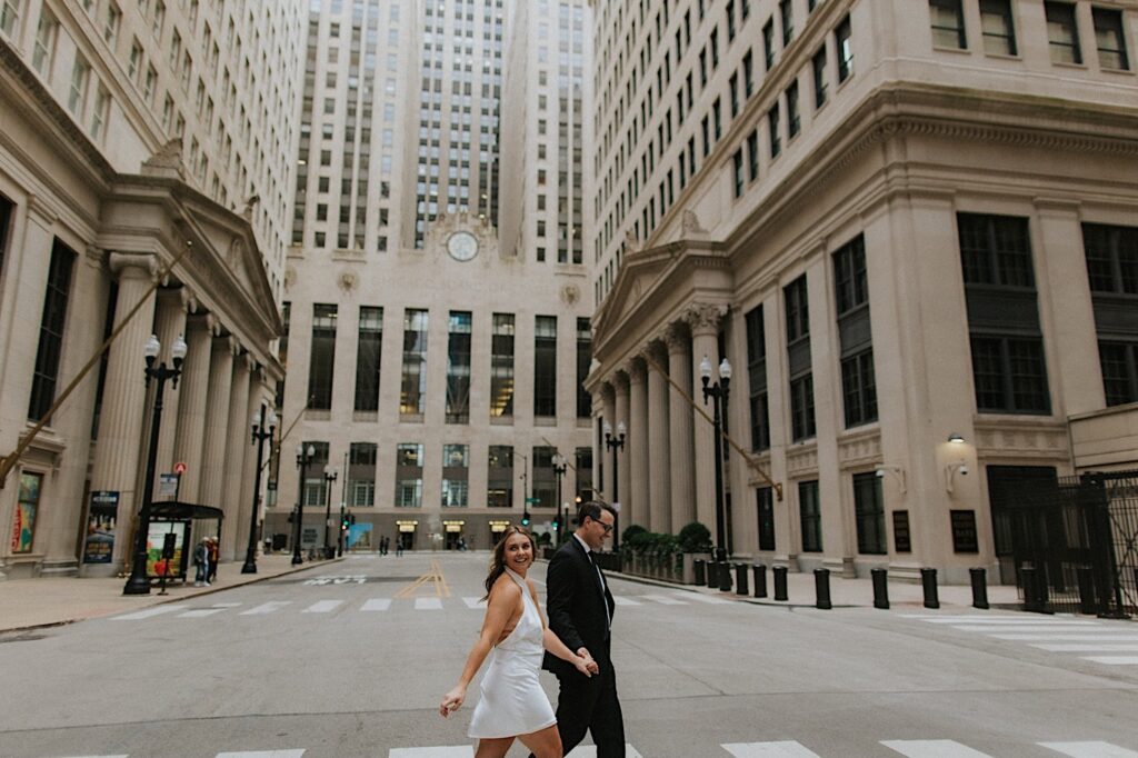 Engagement photo of a couple walking across a street of Chicago together and smiling while holding hands