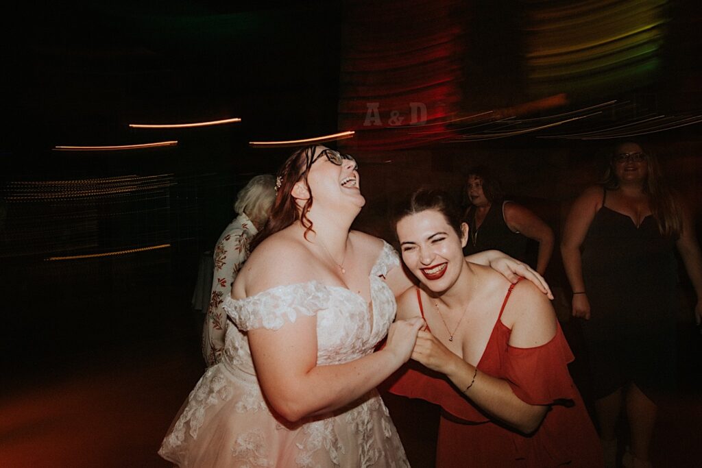 A bride and a guest of her wedding smile and dance with one another indoors during a wedding reception. The photo was taken by a Springfield wedding photographer