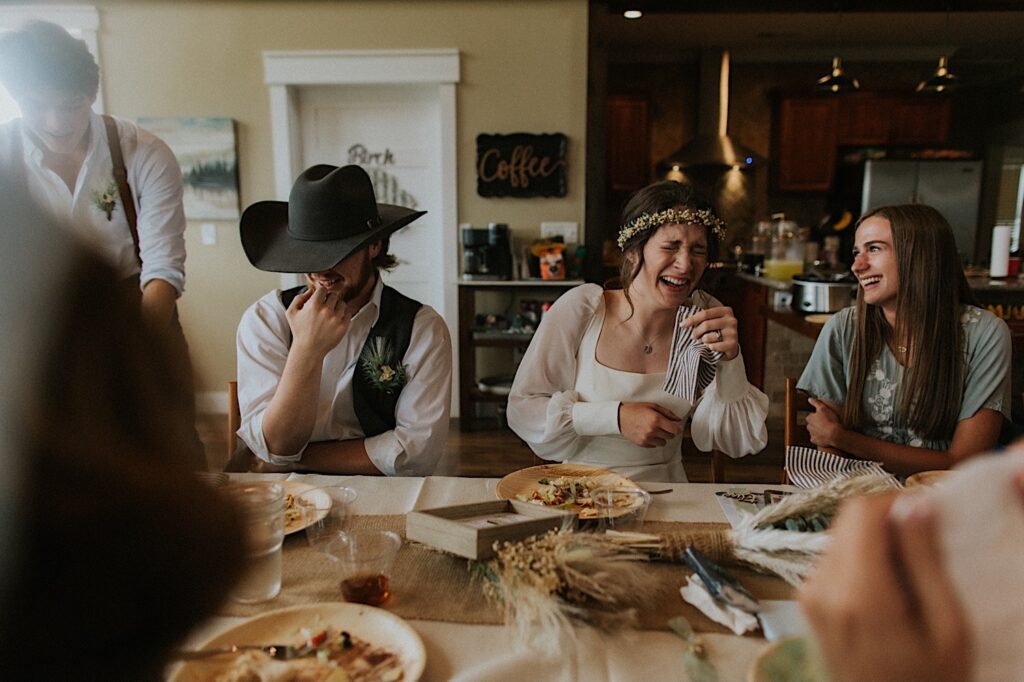A bride and groom smile and laugh while seated at a table having dinner with the guests of their wedding day. The photo was taken by a Springfield wedding photographer