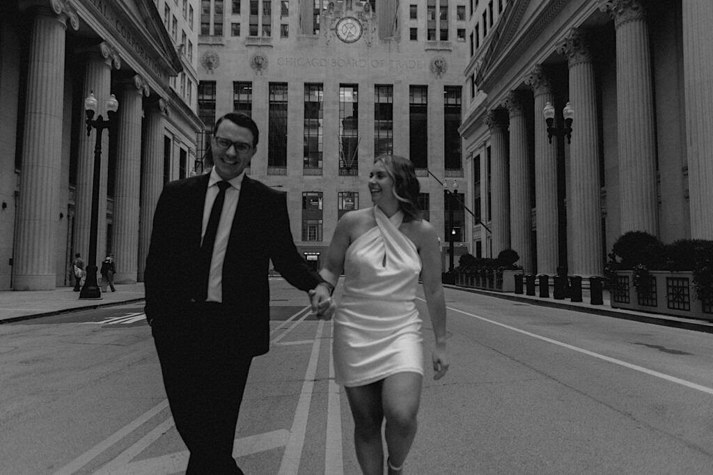 Black and white engagement photo of a couple walking hand in hand towards the camera while in the middle of a street in Chicago