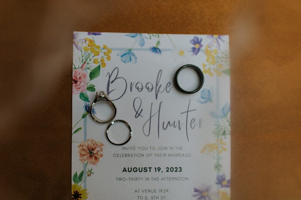 2 wedding rings and an engagement ring rest on top of a wedding invitation