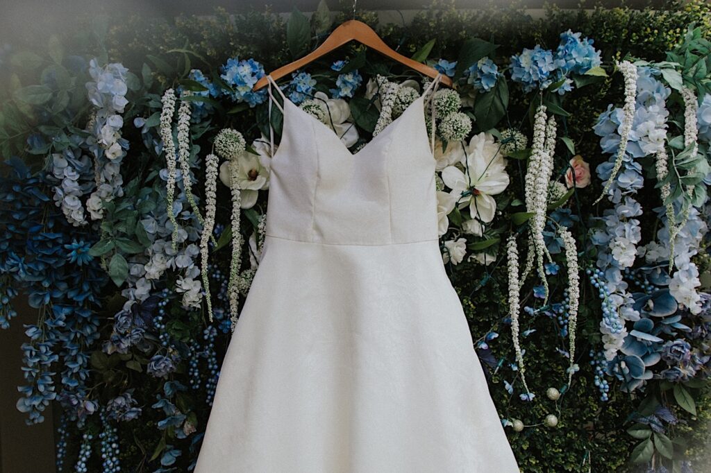 A wedding dress hangs on a wall of blue and white flowers