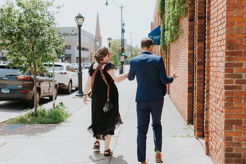 A groom walks alongside a photographer outside of a brick building