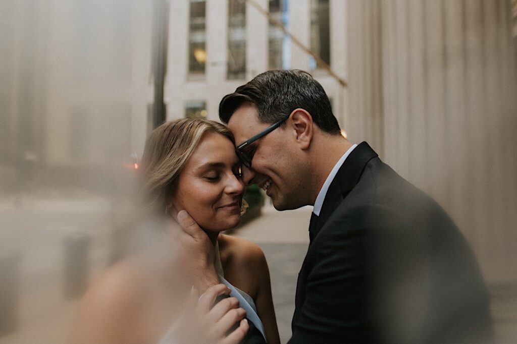 A couple smiles while touching foreheads together as they stand on a street of Chicago while taking engagement photos