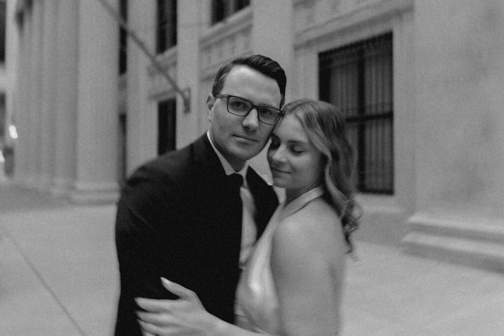 Black and white engagement photo of a couple embracing one another while in Chicago, the man is looking at the camera while the woman has her eyes closed