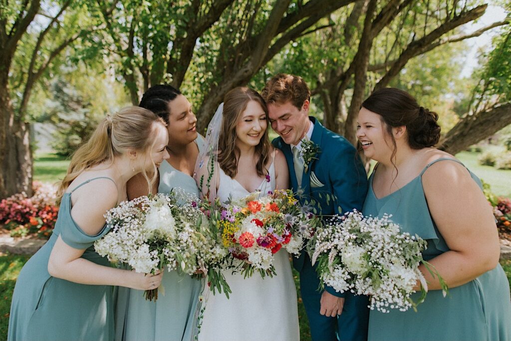 A bridesmaid smiles with the 4 members of her wedding party around her as they all hold their flower bouquets together