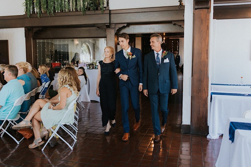 A groom and his parents walk into the indoor space of Venue 1929 in Springfield for the beginning of a wedding ceremony