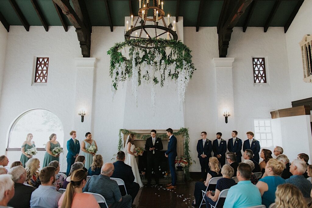 An indoor wedding ceremony takes place at Venue 1929 in Springfield, flowers hang from the huge chandelier in the center of the room