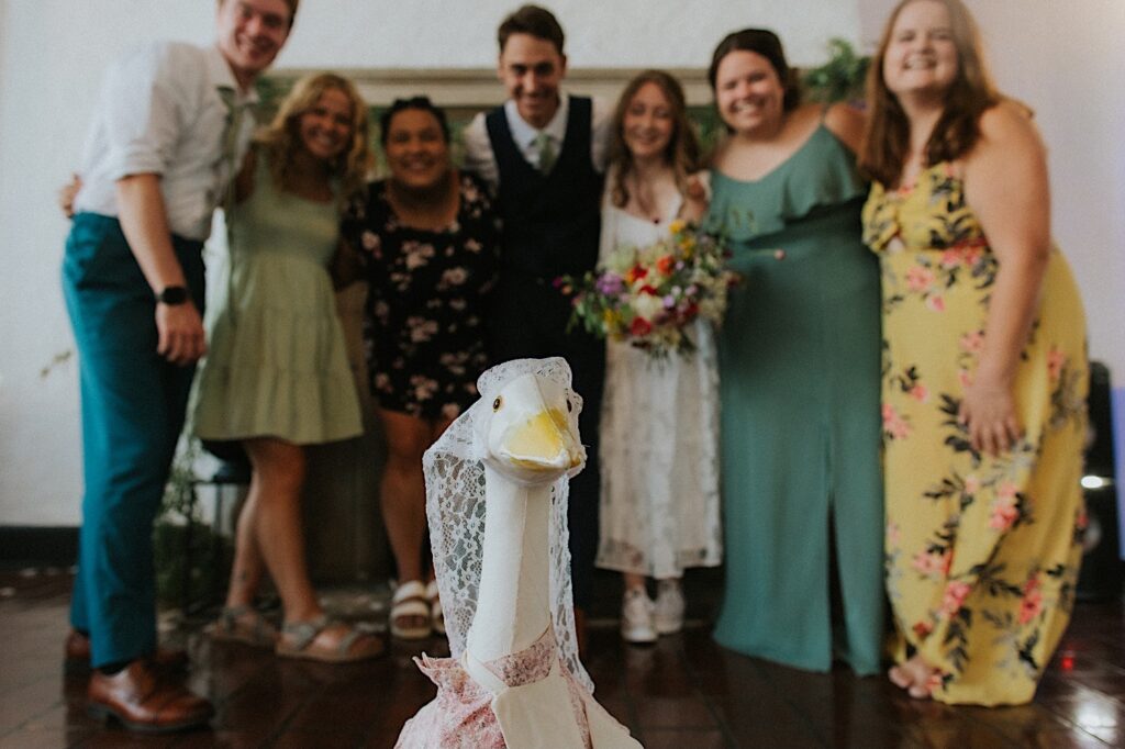 A bride and groom stand with guests of their wedding with a sculpture of a goose in the middle of them during their indoor wedding reception at Venue 1929 in Springfield