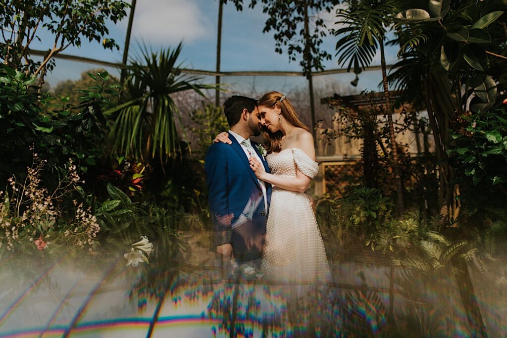 A man and woman embrace while looking at one another and touching foreheads together while in a greenhouse taking portraits on their elopement day