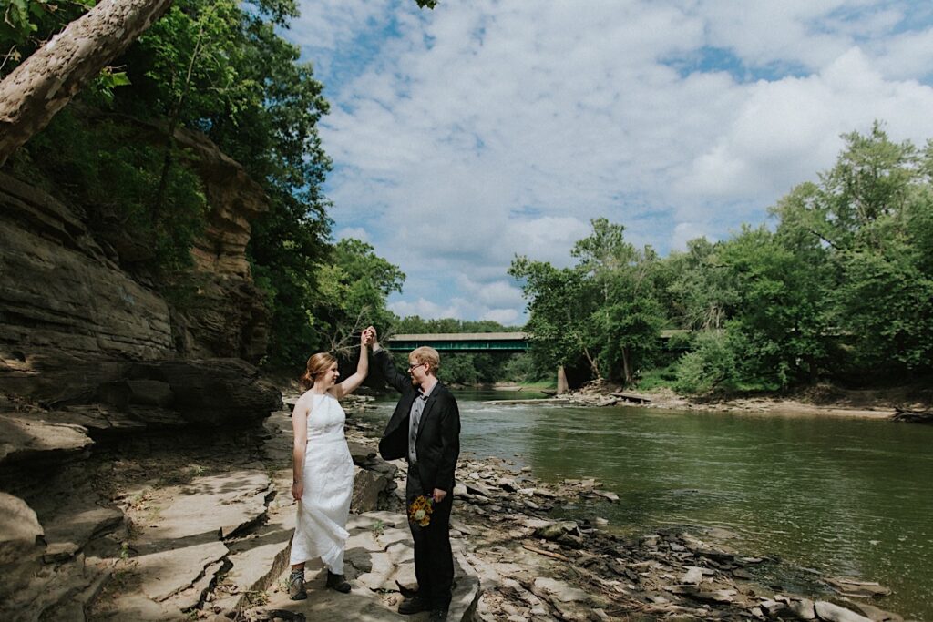 A bride and groom dance together on the shore of a river while taking elopement portraits
