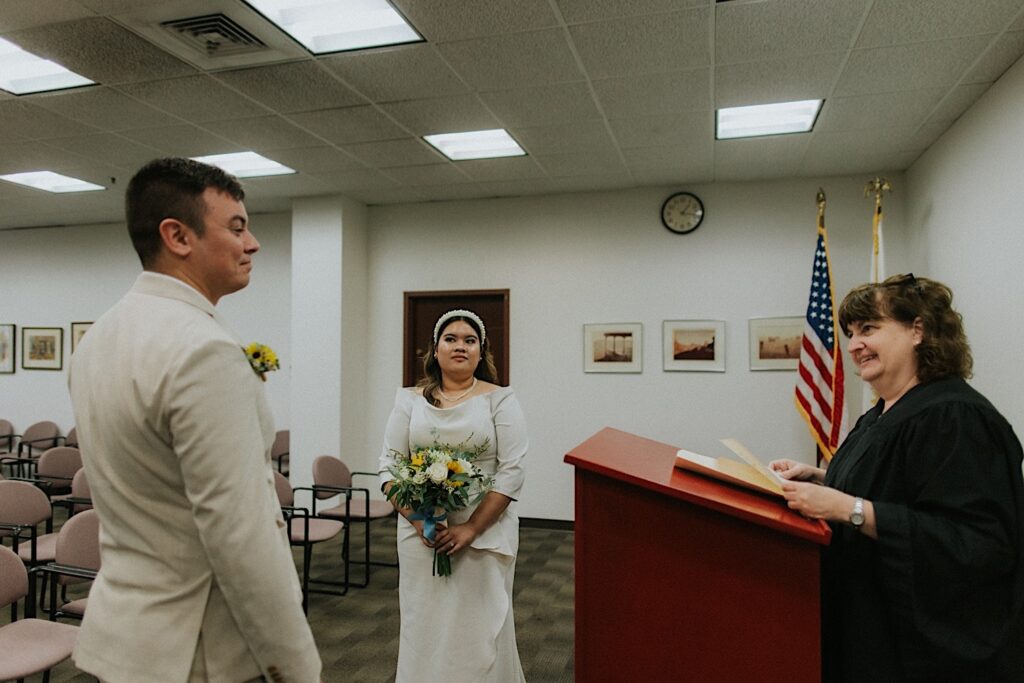 A bride and groom face one another while an officiant speaks to them during their wedding ceremony at the Sangamon County Courthouse