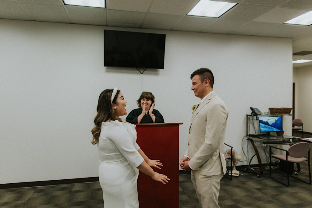 A bride exclaims to the groom as their officiant claps for them during their wedding ceremony at the Sangamon County Courthouse