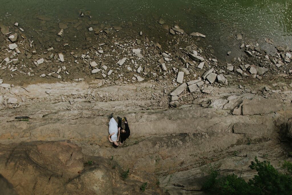 Aerial photo of a bride and groom sitting together on the shore of a river during their elopement day
