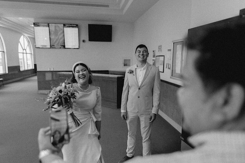 Black and white photo of a bride and groom smiling as a guest of their intimate wedding at the Sangamon County Courthouse facetimes one of their friends