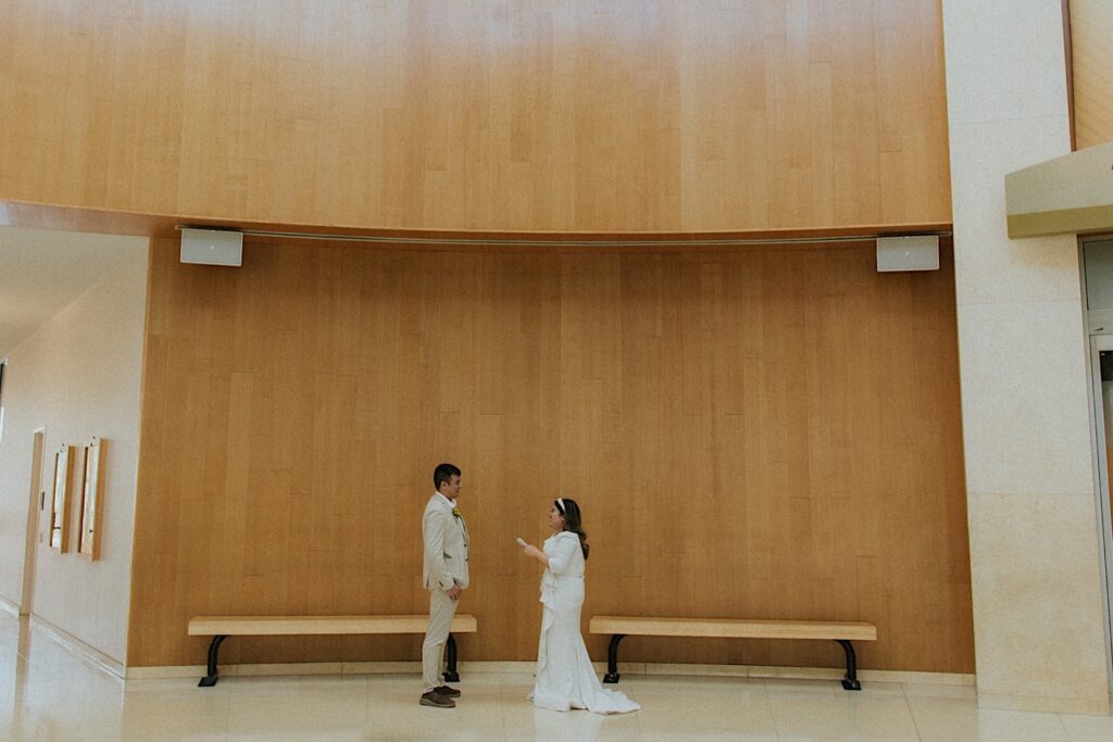 A bride reads her vows to the groom standing in front of her in an empty room on their elopement day