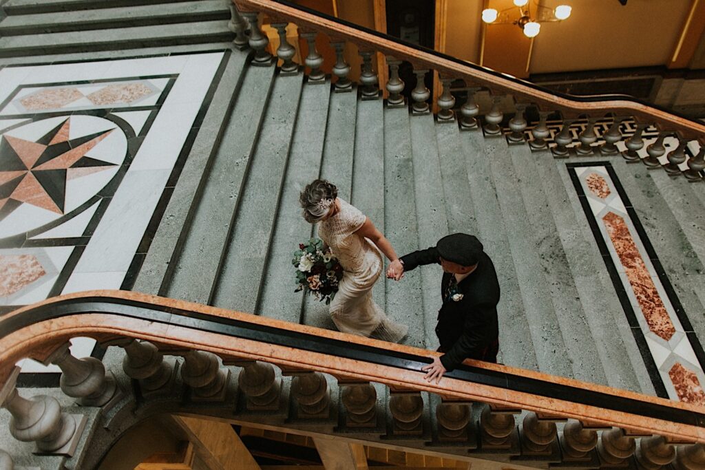 A bride leads the groom by the hand up a set of marble stairs during their elopement day