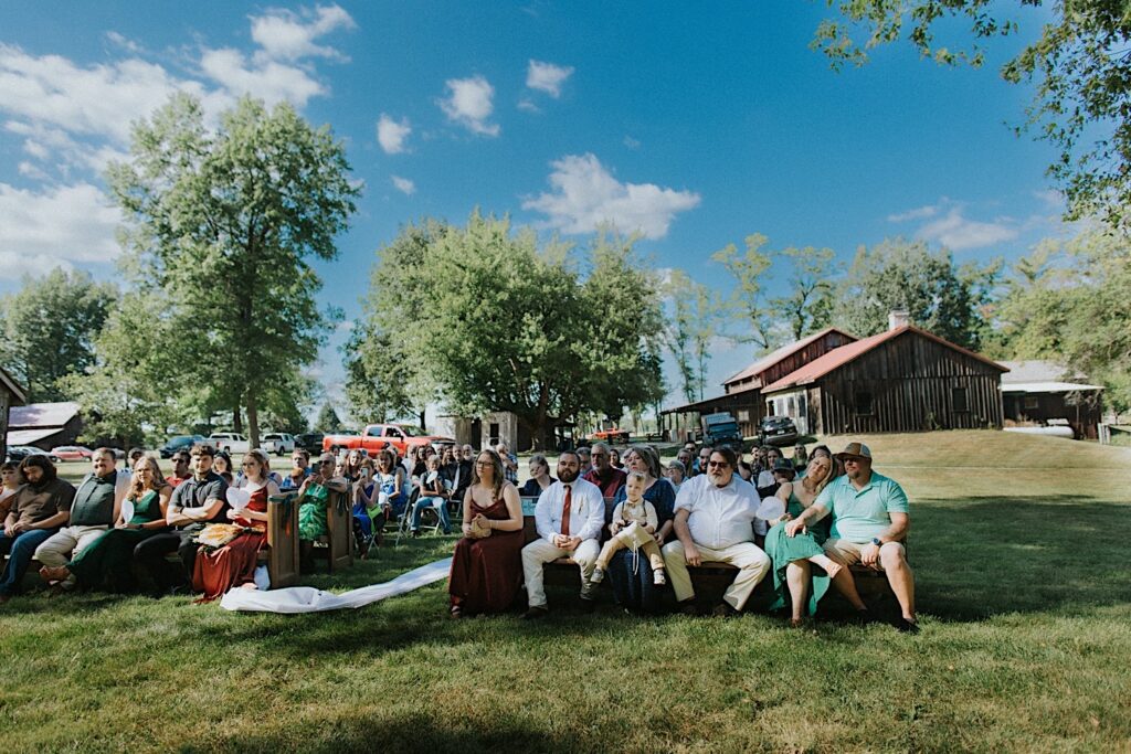 Guests of an outdoor wedding ceremony at the Clayville Historic Site sit and watch as the ceremony takes place