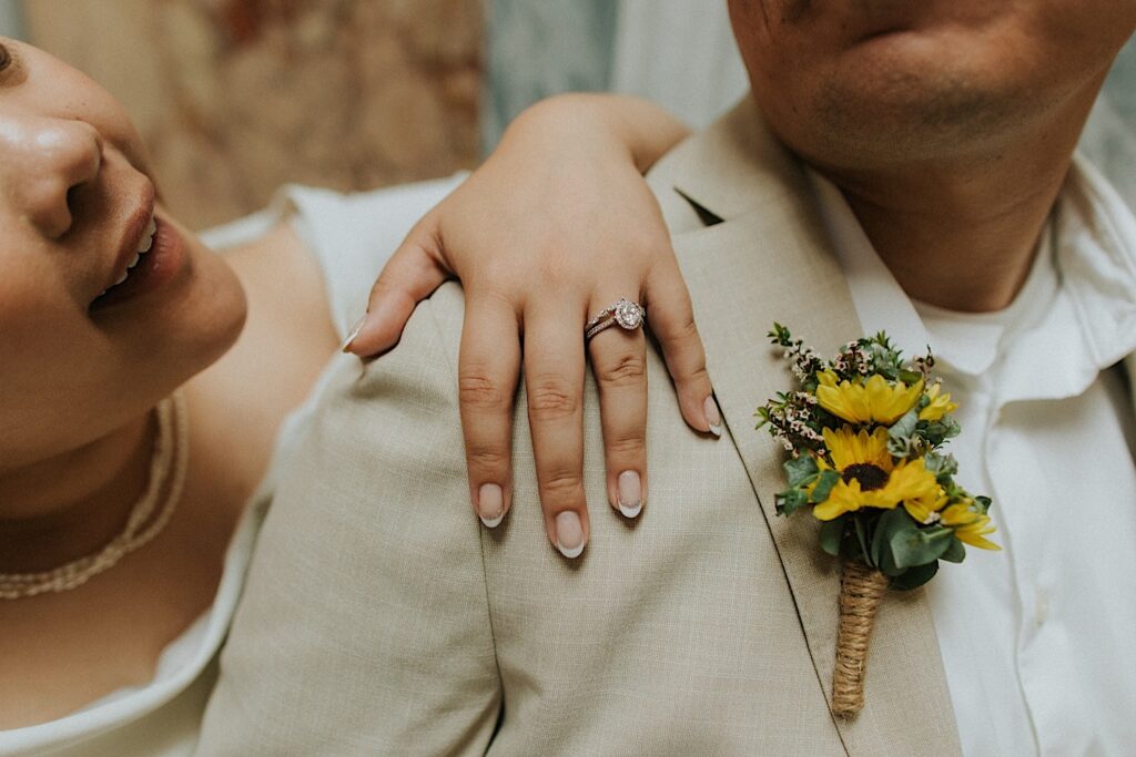 A bride puts her hand on the grooms shoulder showing off her wedding ring as she stands behind him
