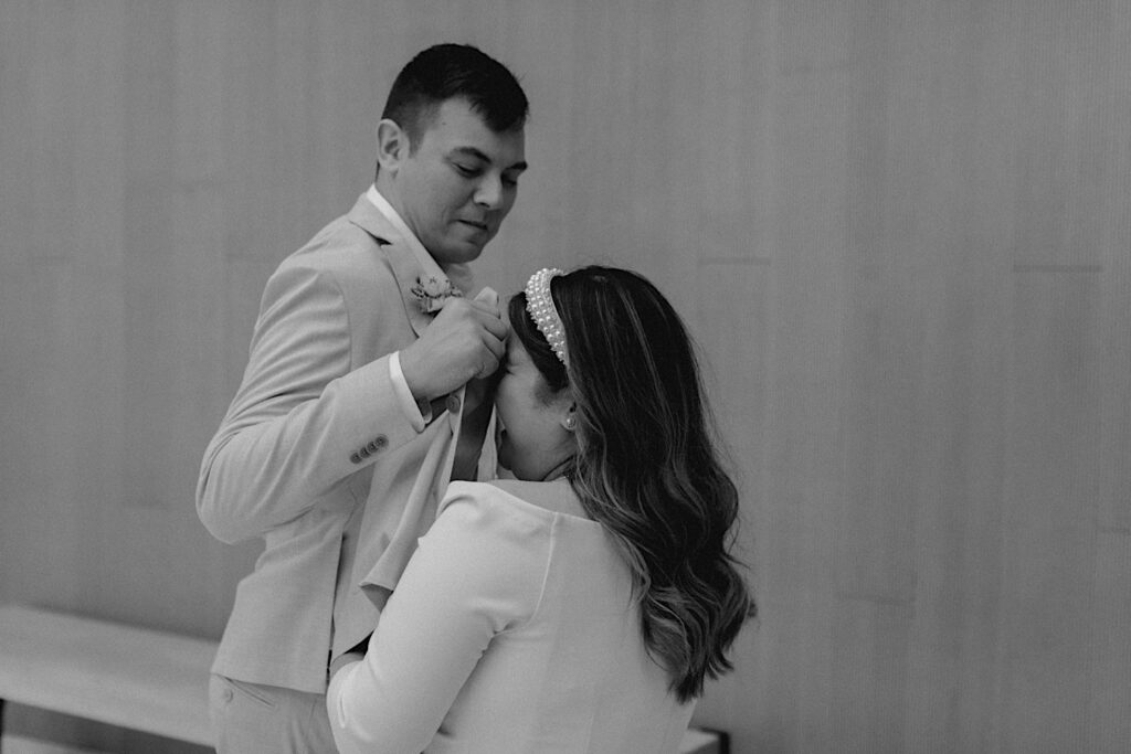 Black and white photo of a bride laughing as the groom wipes a tear from her face with his suit coat
