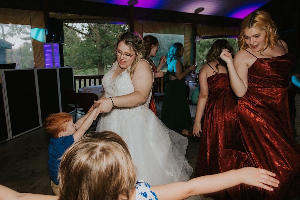 A bride dances with a young boy alongside members of her wedding party during her indoor wedding reception at the Clayville Historic Site