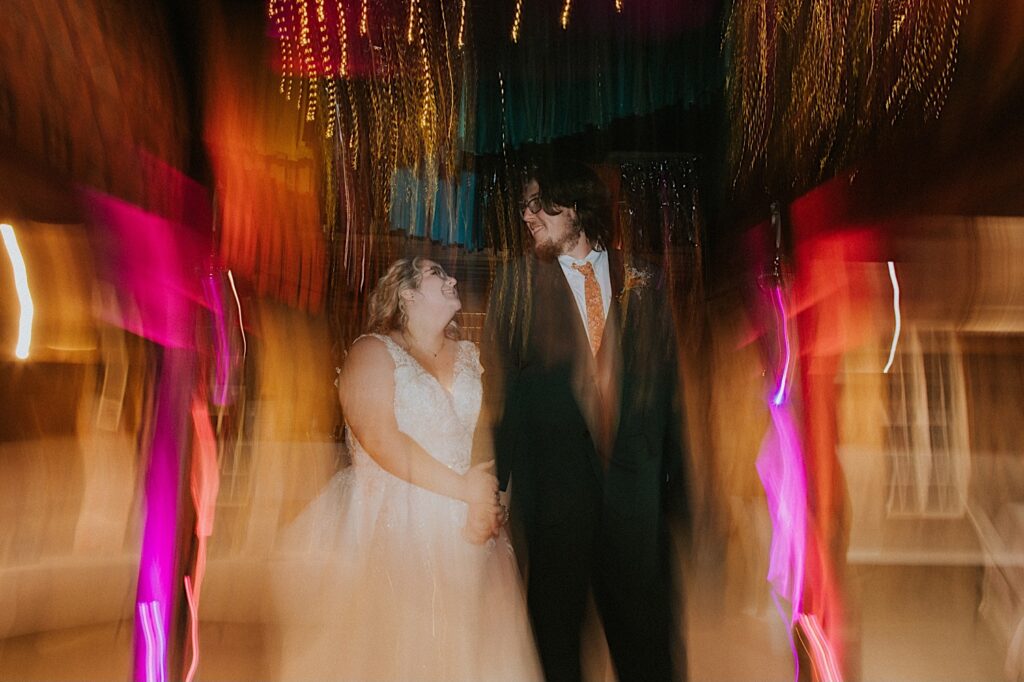 A bride and groom hold hands and look at one another while light distorts around them during their indoor wedding reception at the Clayville Historic Site