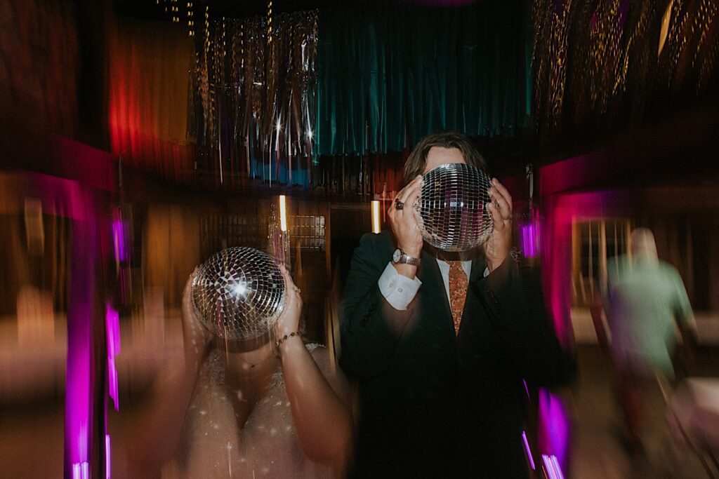 A bride and groom hold disco balls in front of their faces while light distorts around them during their indoor wedding reception at the Clayville Historic Site