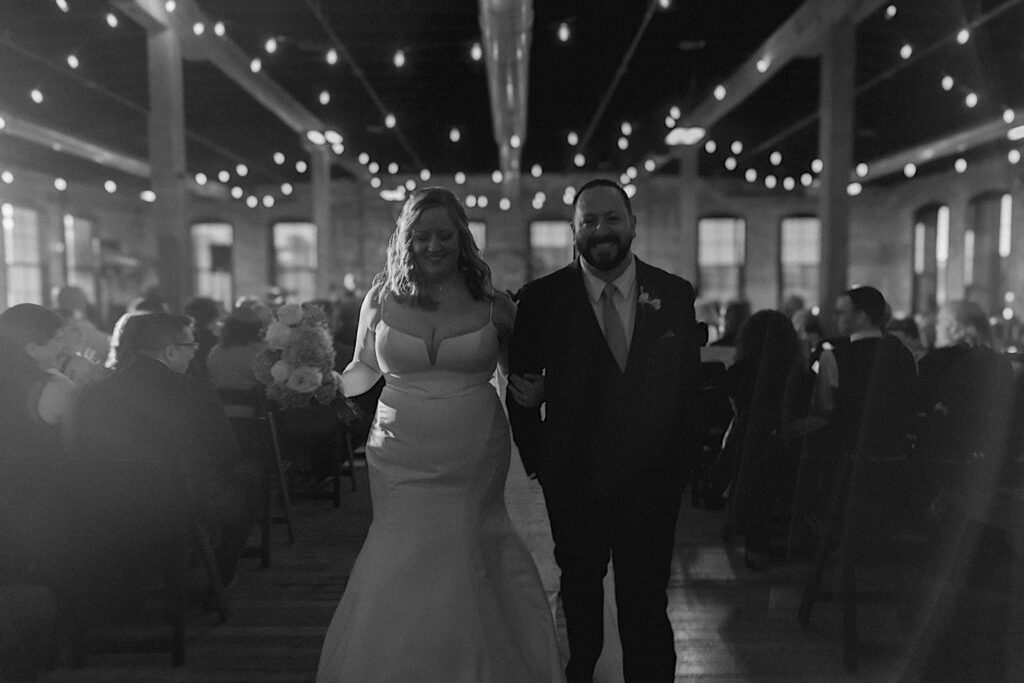 Black and white photo of a bride and groom walking down the aisle together after their wedding ceremony at their venue in Bloomington, Illinois