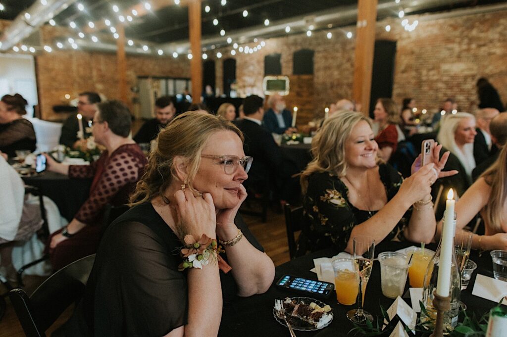 Guests of an indoor wedding reception at a venue in Bloomington, Illinois sit next to one another and smile