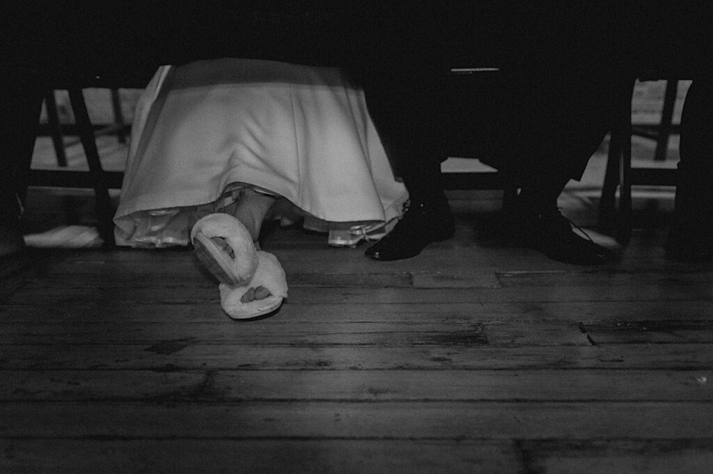 Black and white photo of a bride and groom's legs under the table of their wedding reception