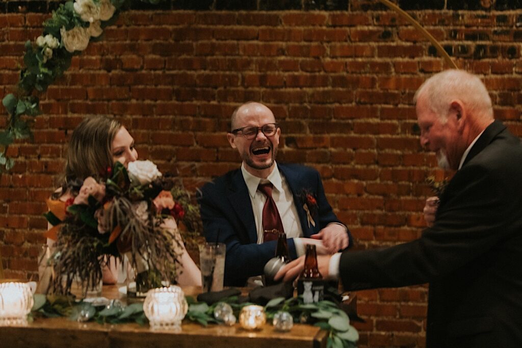 A bride and groom laugh as they sit at their sweetheart table after the bride's father just gave a speech during their intimate wedding reception at Reality on Monroe