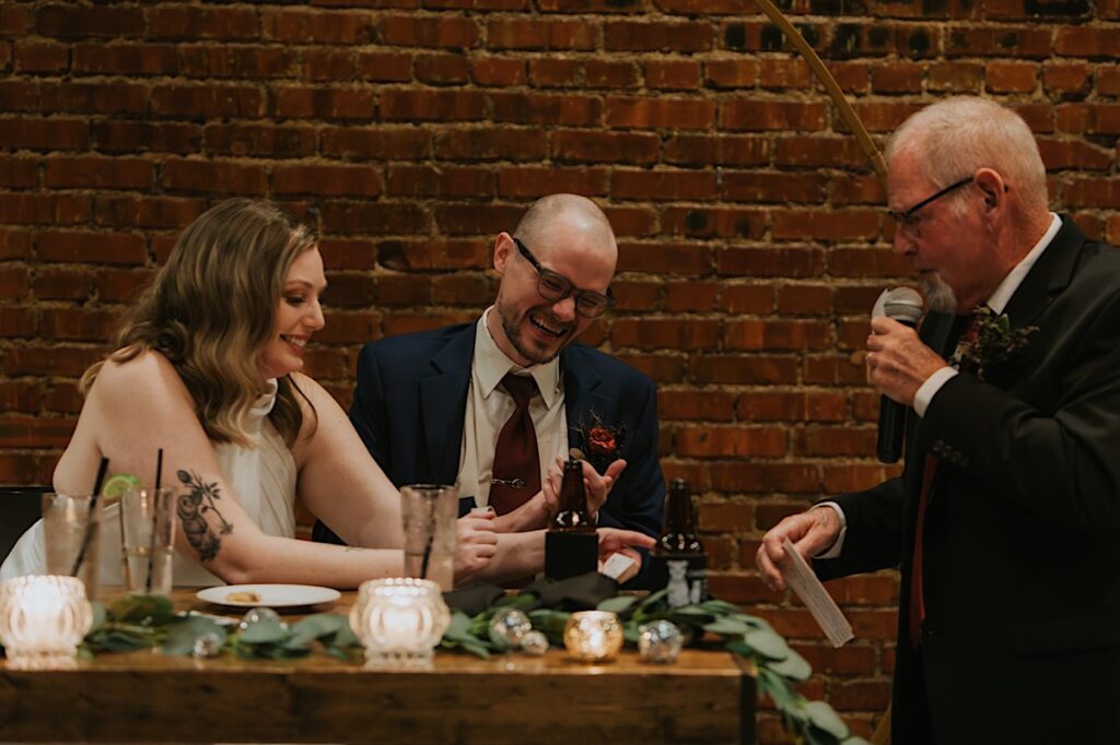 A bride and groom laugh while talking with the bride's father during his speech at their intimate wedding reception at Reality on Monroe