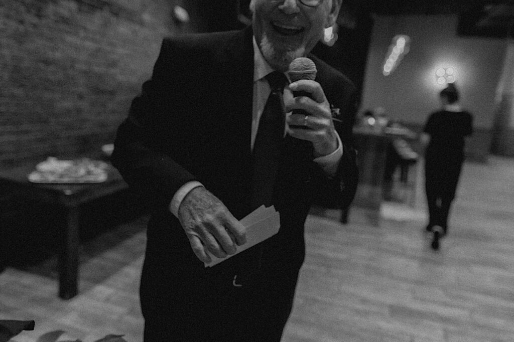 Black and white photo of the father of the bride smiling as he gives a speech during an intimate wedding reception at Reality on Monroe