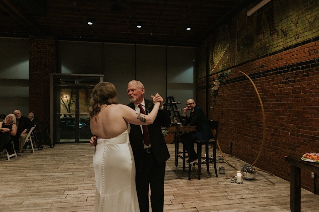 A bride dances with her father as the groom watches during their intimate wedding reception at Reality on Monroe