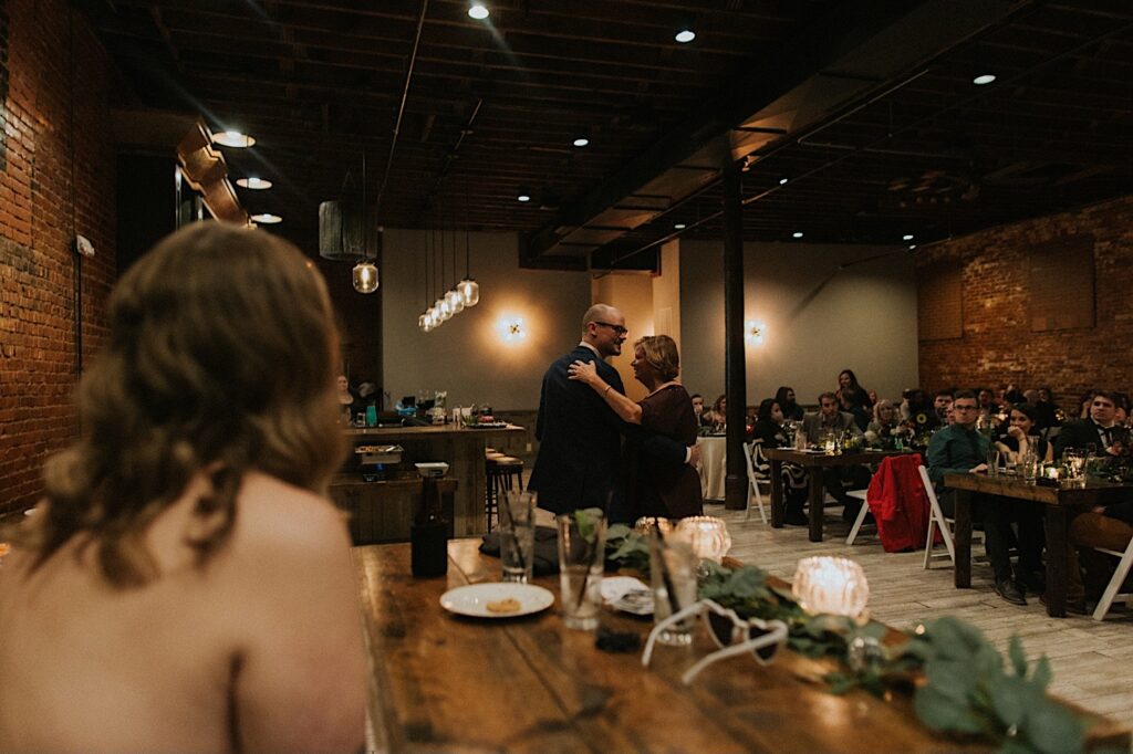 A bride watches as the groom and his mother share a dance together during their intimate wedding reception at Reality on Monroe