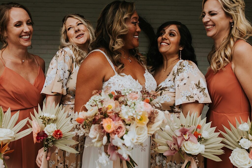 A bride smiles while surrounded by 4 members of her wedding party as they all smile at her