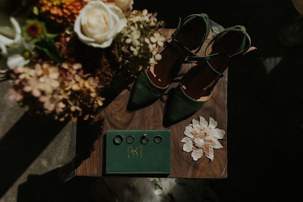 Top down photo of a wedding flatlay consisting of shoes, a vow book, wedding rings, and florals