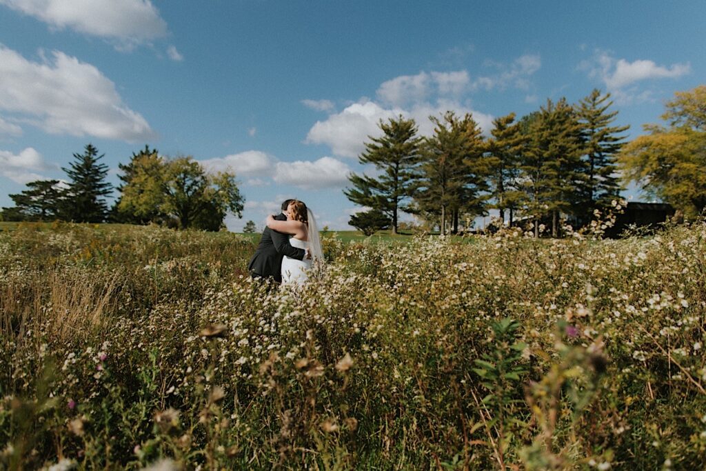 A bride and groom hug one another while in the middle of a field after their first look