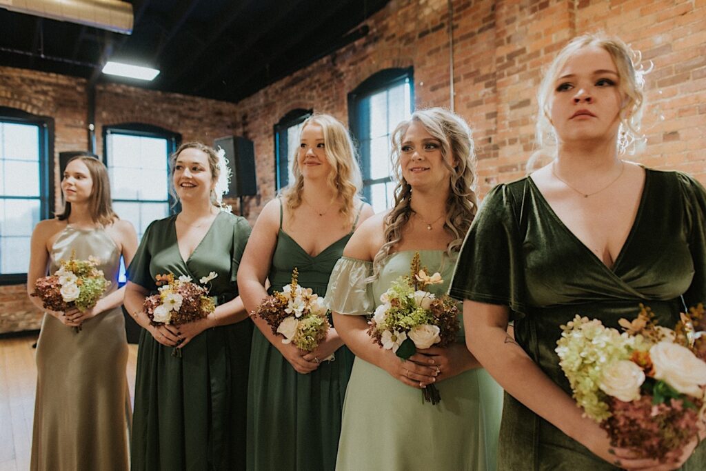 5 bridesmaids stand side by side and look towards the bride entering her the ceremony space of her wedding at Trailside Event Center