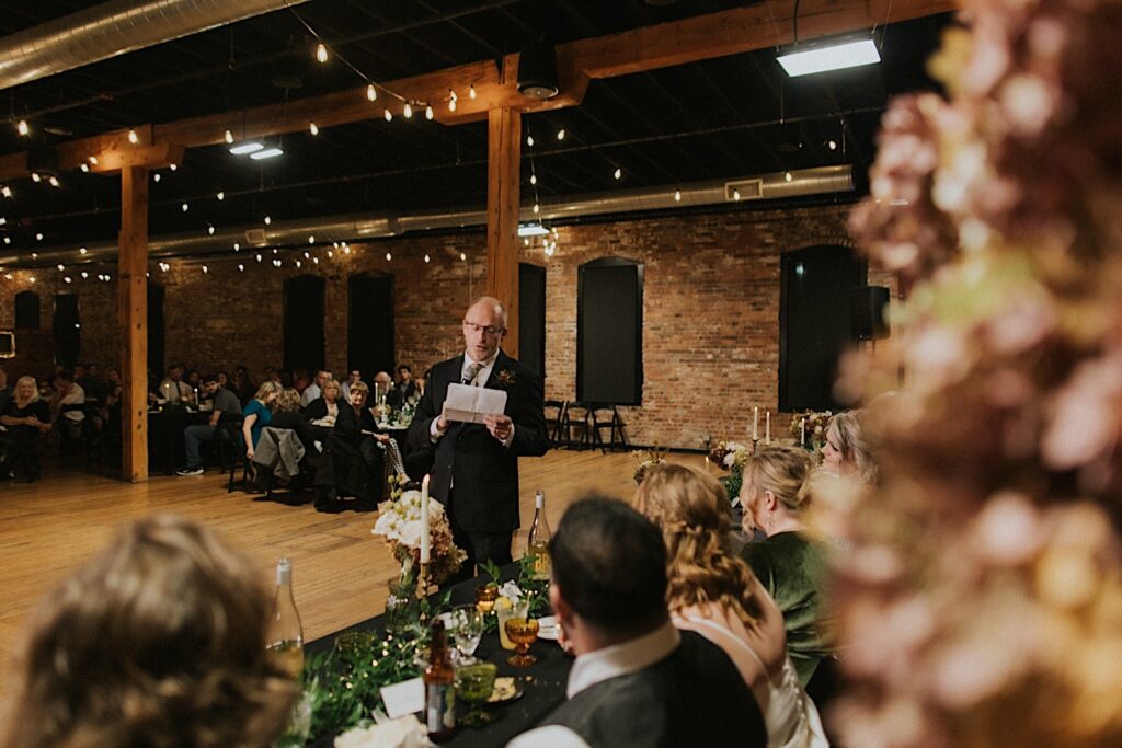 A father gives a speech during a wedding reception at Trailside Event Center as the bride and groom listen