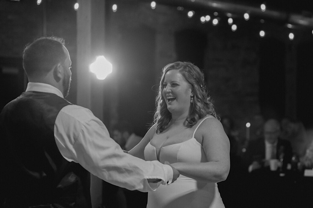Black and white photo of a bride smiling while dancing with the groom during a wedding reception at Trailside Event Center