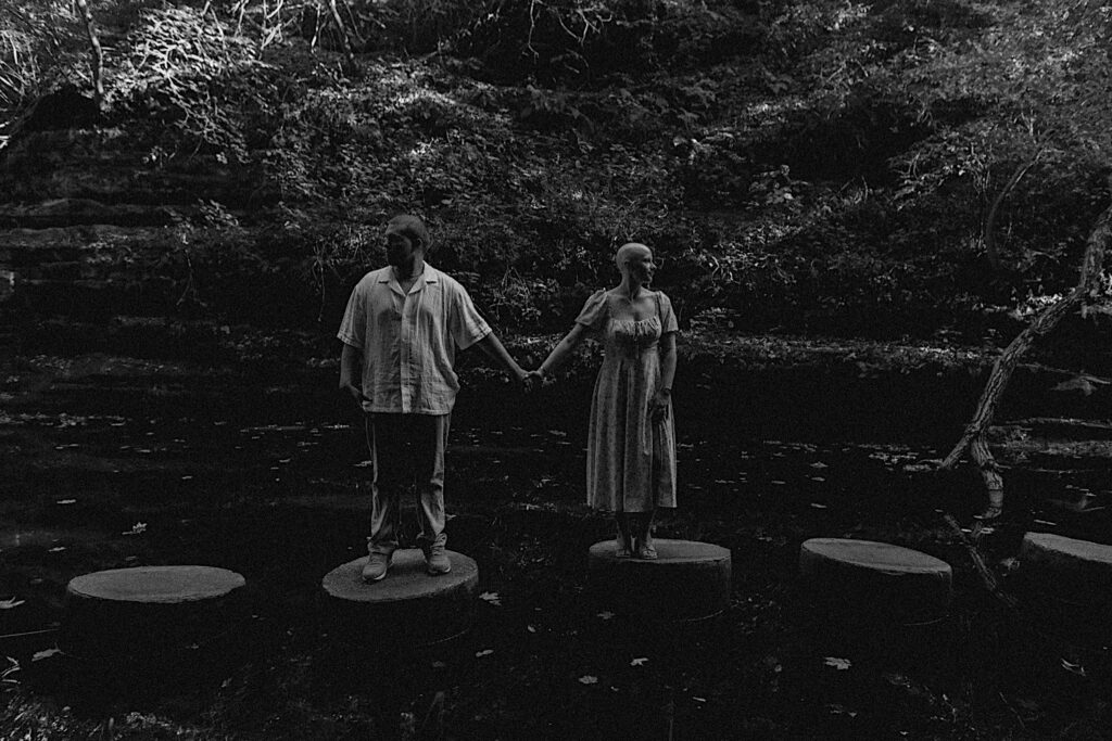 Black and white photo from an engagement session at Matthiessen State Park in Central Illinois where a man and woman hold hands while standing on rock pillars and look in opposite directions