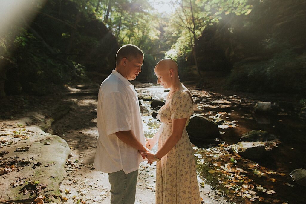 A couple hold hands during their engagement session at Matthiessen State Park in Central Illinois and look down as the sun shines upon them