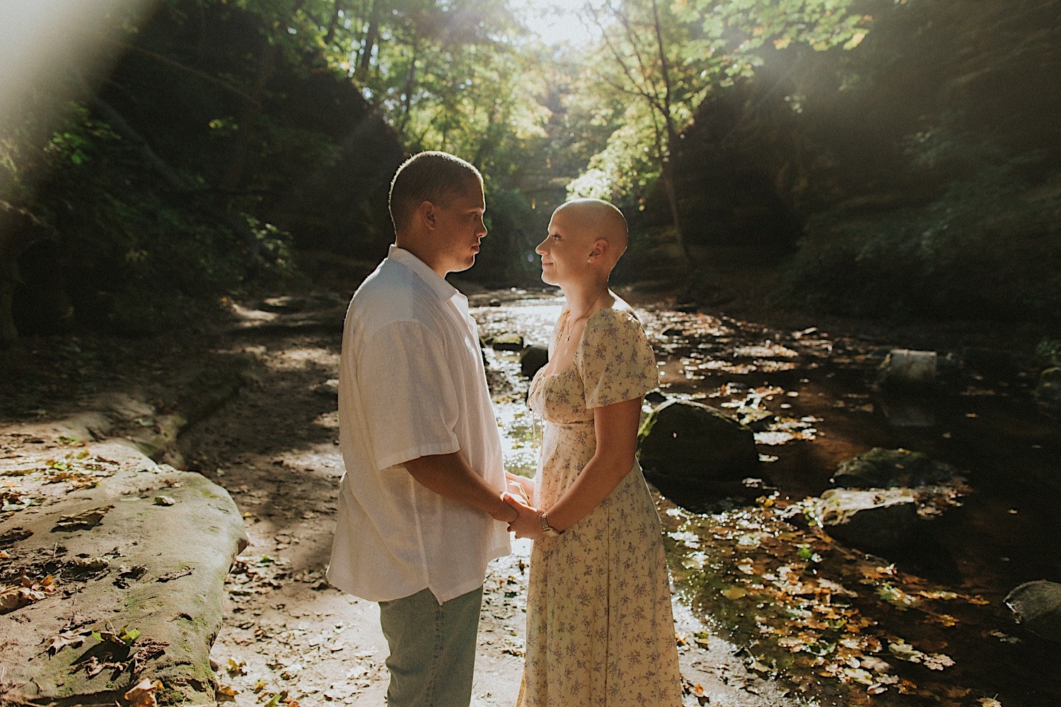 During their engagement session a couple smile at one another and hold hands while next to a creek in Matthiessen State Park of Central Illinois