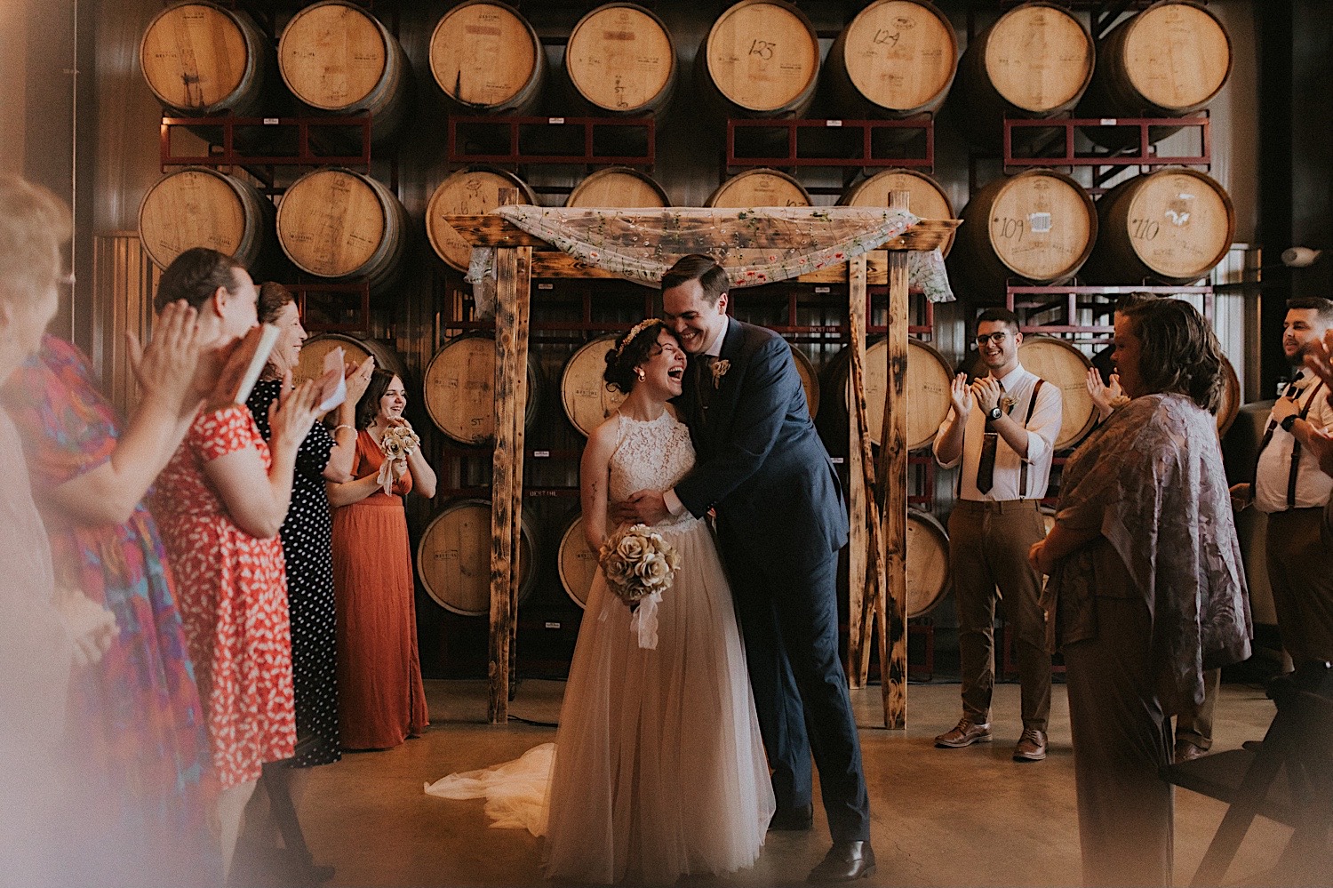 A bride and groom hug one another while exiting their wedding ceremony at their venue, The Barrel Room at the Destihl Brewery in Central Illinois