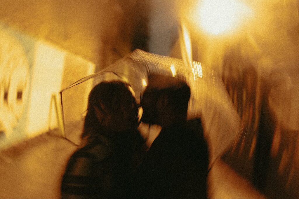 Blurry picture of a couple kissing in the rain surrounded by yellow lights.